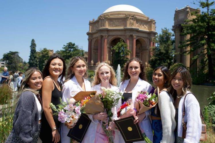 Smiling students wearing white coats in front of the Palace of Fine Arts